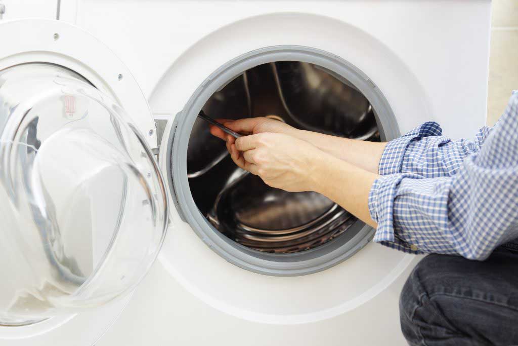 A man in blue overalls fixing a washing machine