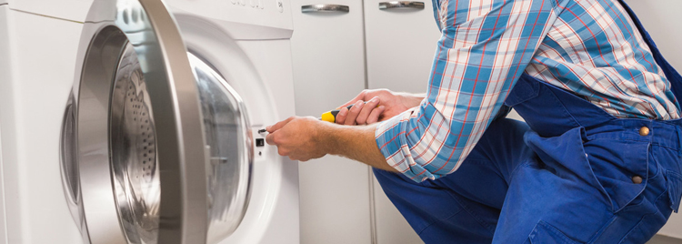 A man in blue overalls fixing a clothes dryer